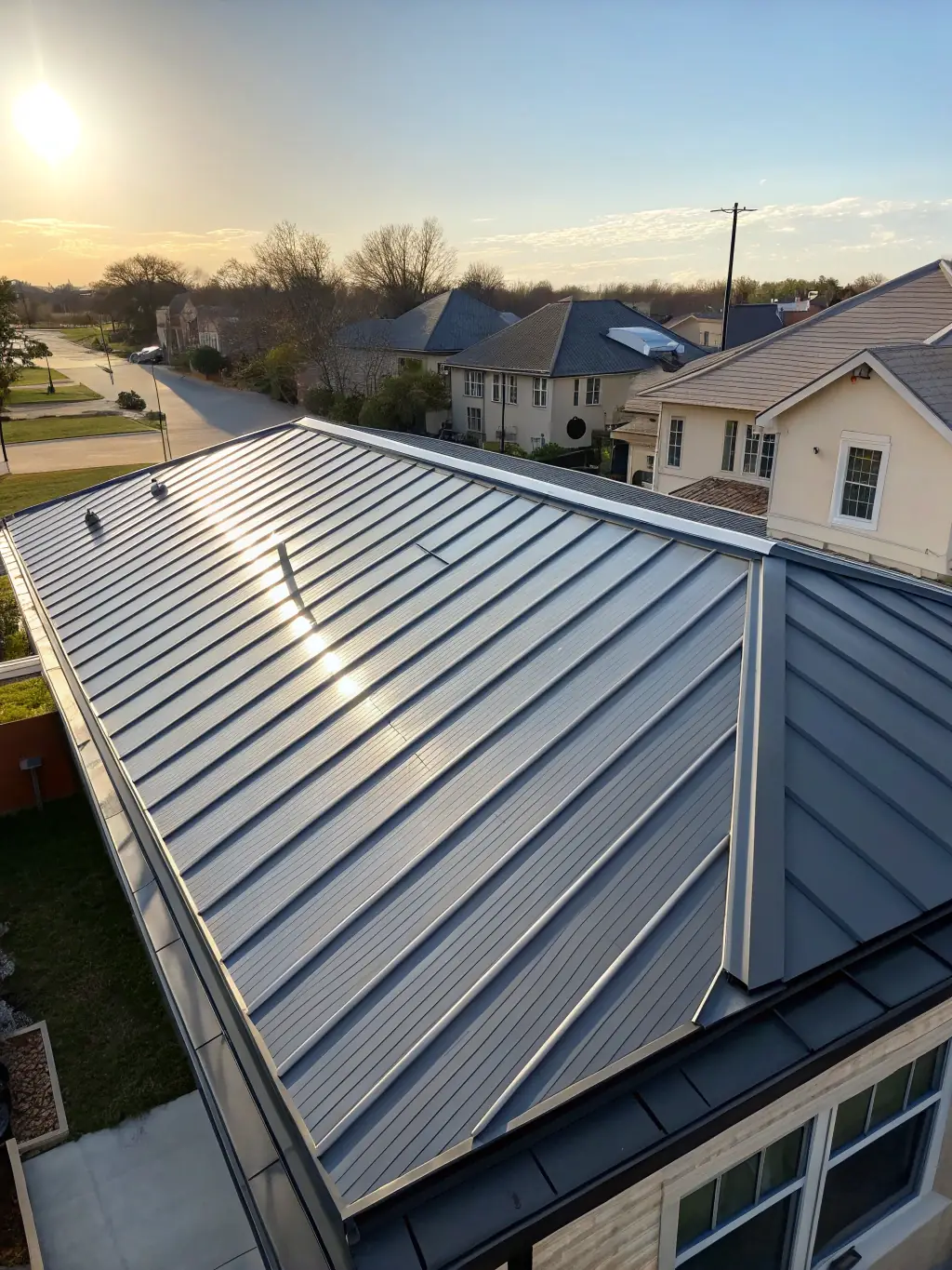 A high-angle shot of a newly installed steel roof on a residential home, highlighting the clean lines and modern aesthetic. The roof is a dark gray color, contrasting with the light-colored siding of the house. The image should convey durability and quality craftsmanship.